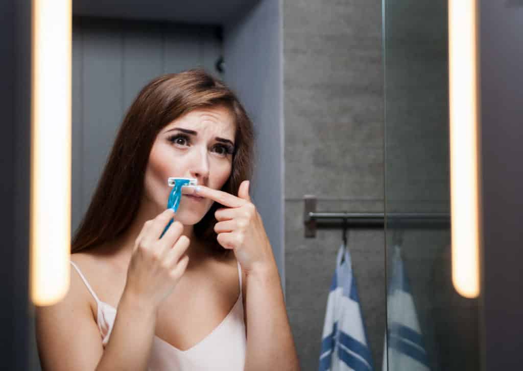 Woman shaving her face to remove facial hair