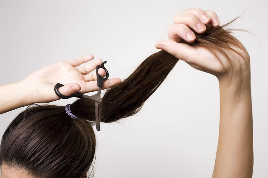 Girl cutting her hair with the ponytail method