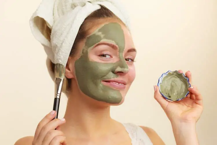 Girl applying clay mask to her face to get rid of oil on her nose and forehead
